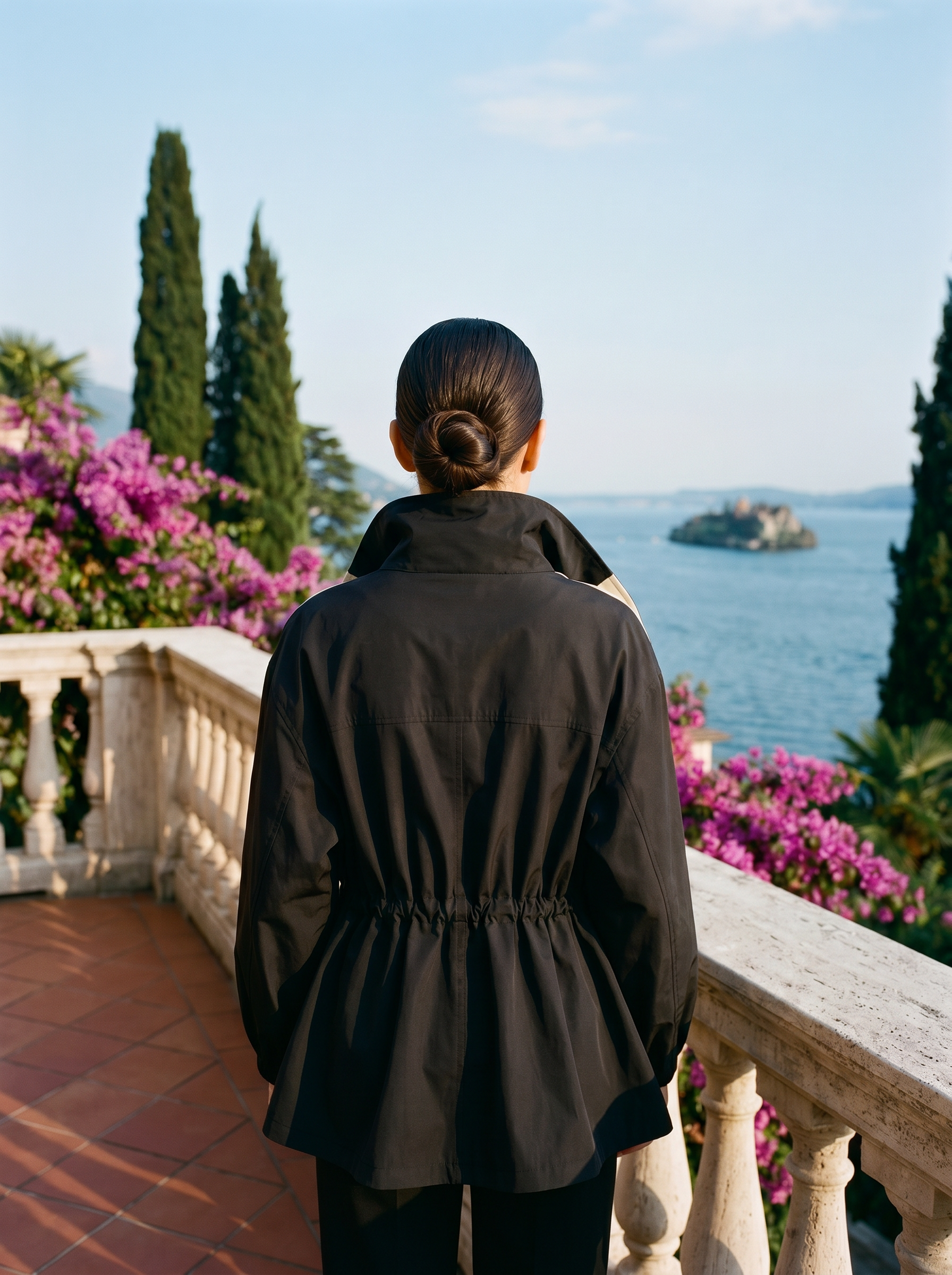 Black draped-collar windbreaker jacket, full body back view on a Lake Como terrace — Aveloire