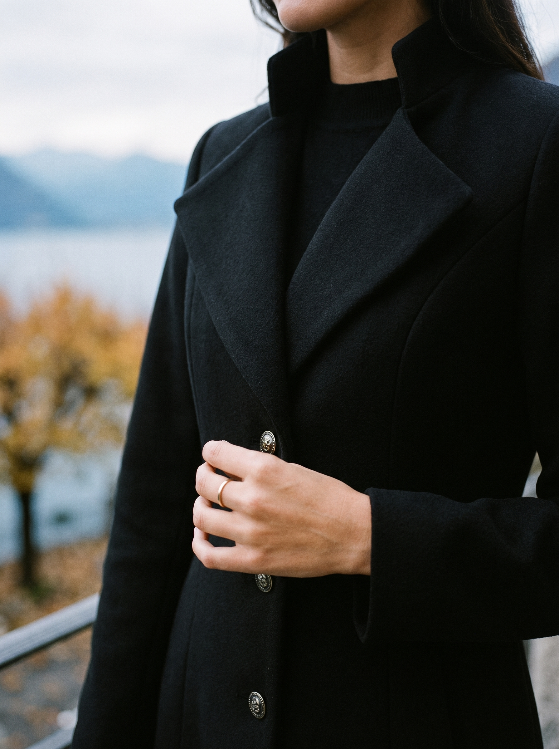 Close-up of the notched lapel and decorative buttons on the black overcoat — Aveloire