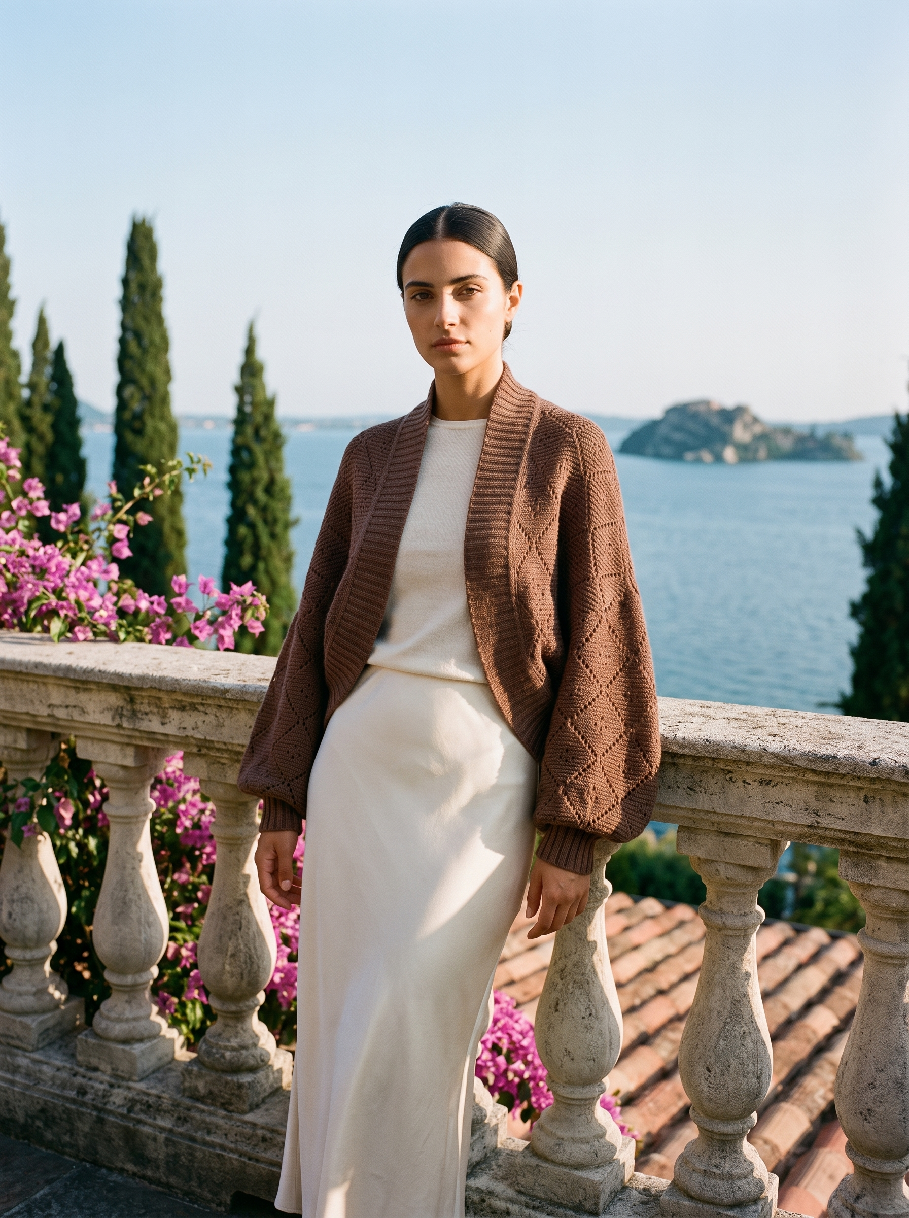 Full-length view of a cocoa brown cropped knit shrug cardigan on a Lake Como terrace — Aveloire