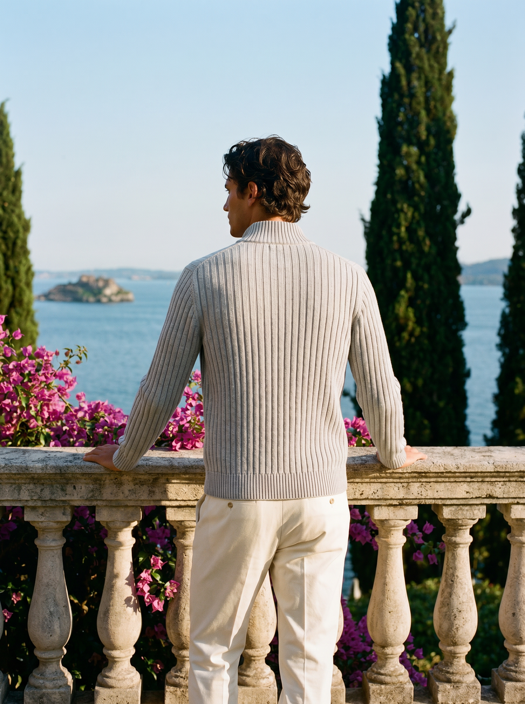 Back view of a light gray ribbed cotton full-zip cardigan worn on a Mediterranean terrace — Aveloire