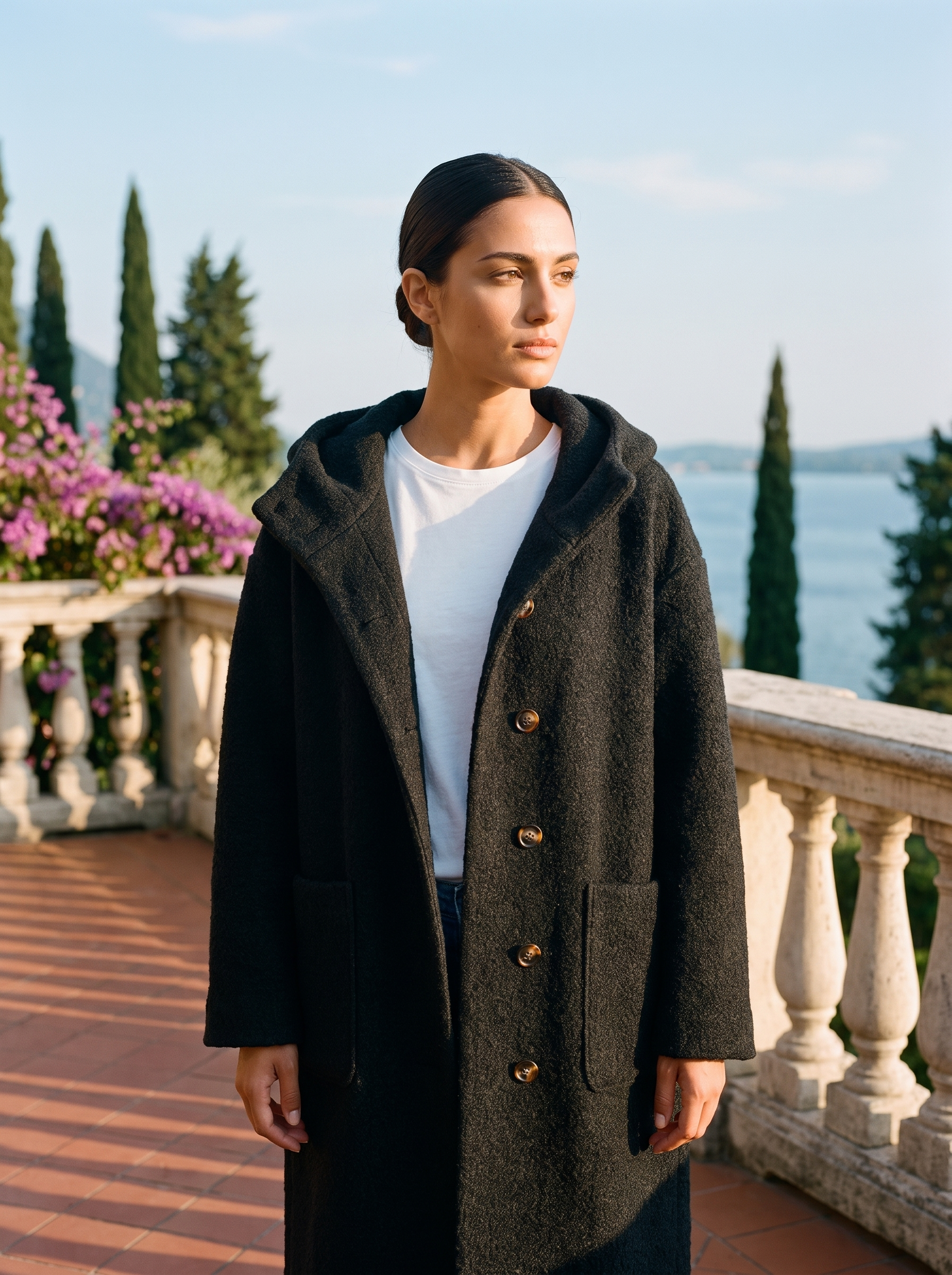 Woman wearing a black hooded wool coat on a terrace overlooking Lake Como — Aveloire