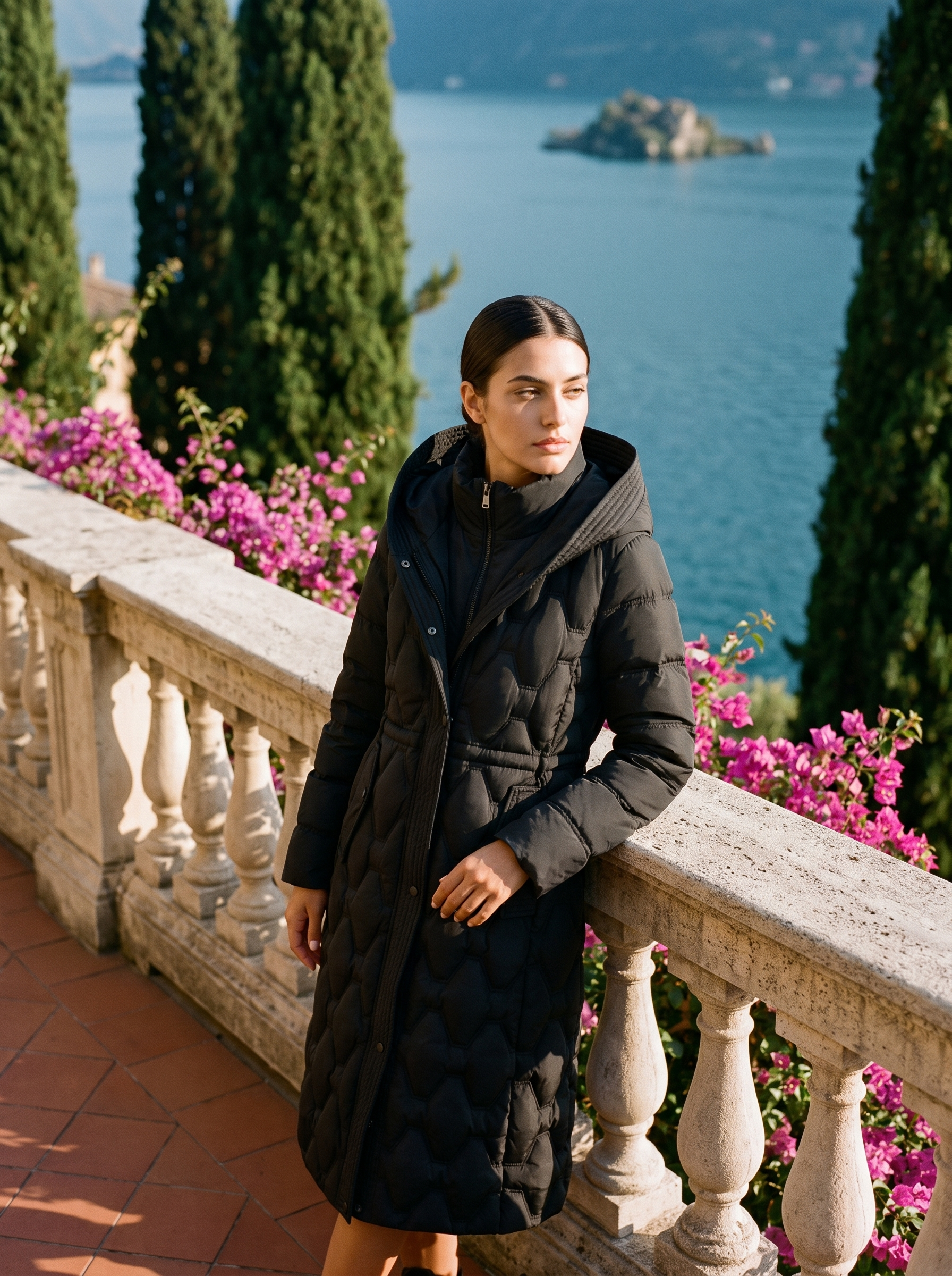 Woman wearing black onion-quilted longline hooded puffer coat on a Lake Como terrace
