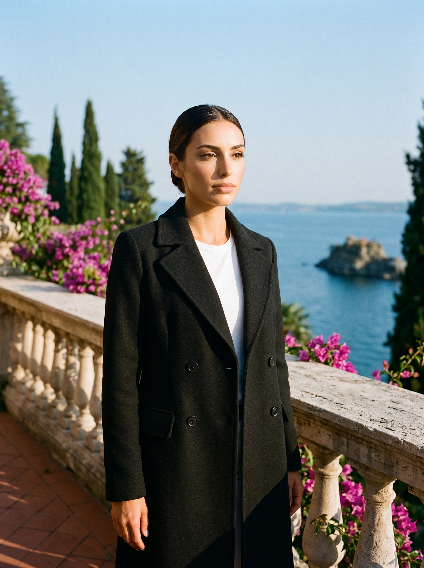 Woman wearing a black wool overcoat on a terrace overlooking Lake Como — Aveloire