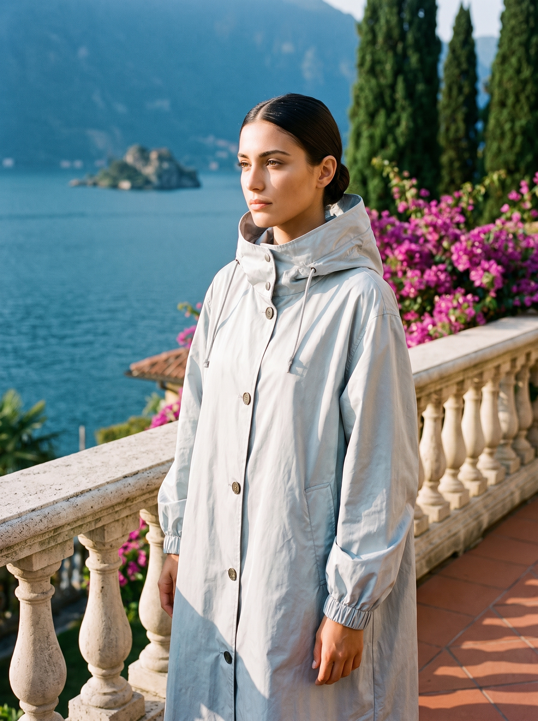 Woman wearing pale light blue water-repellent hooded raincoat on a Lake Como terrace