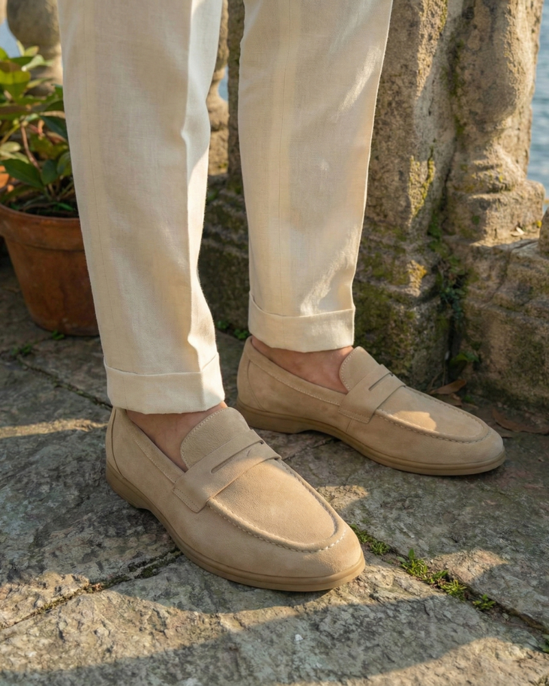 Men’s beige leather slip-on loafers styled on feet with tailored trousers