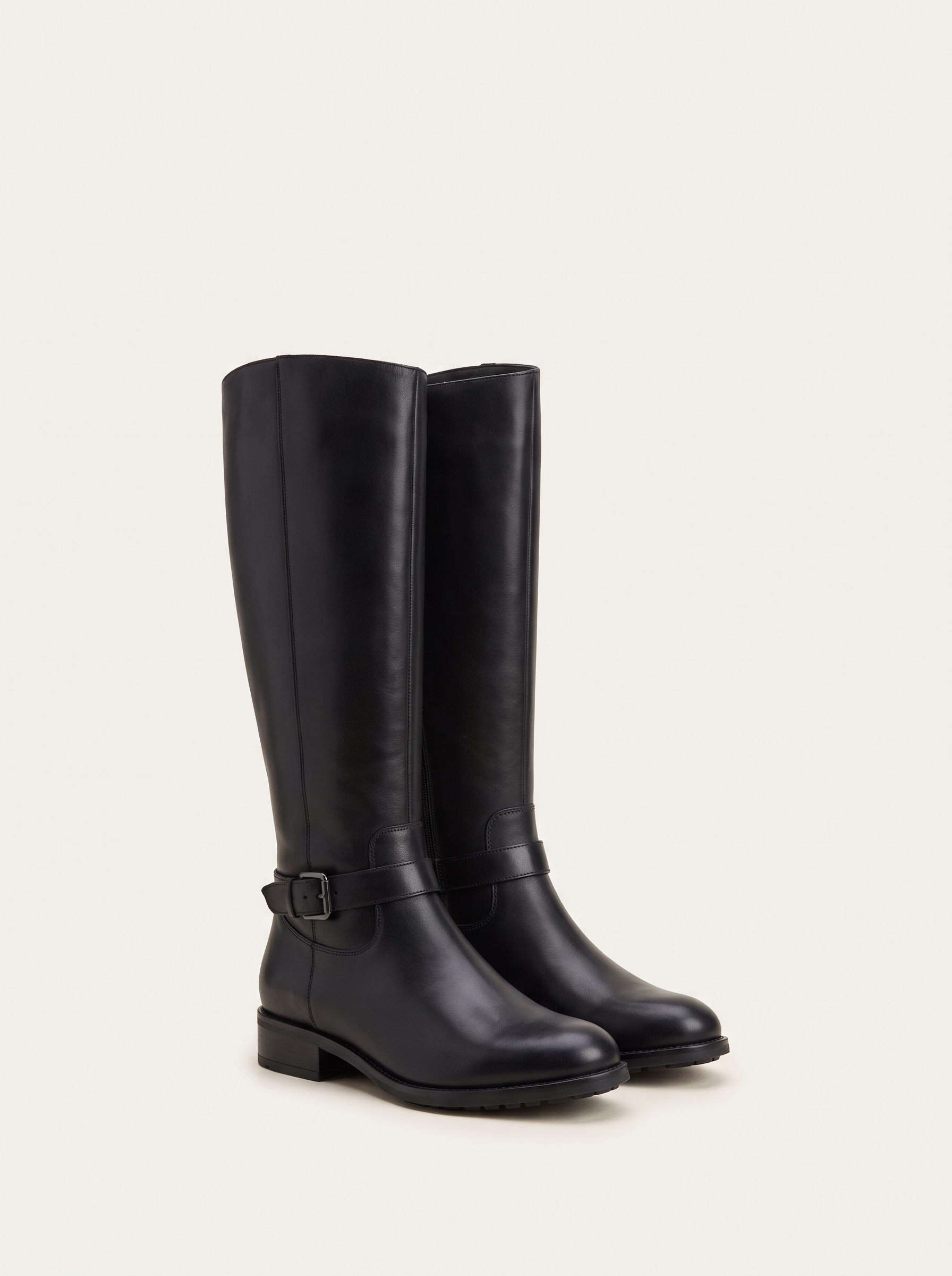 Pair of black buckled riding knee high boots on off-white background