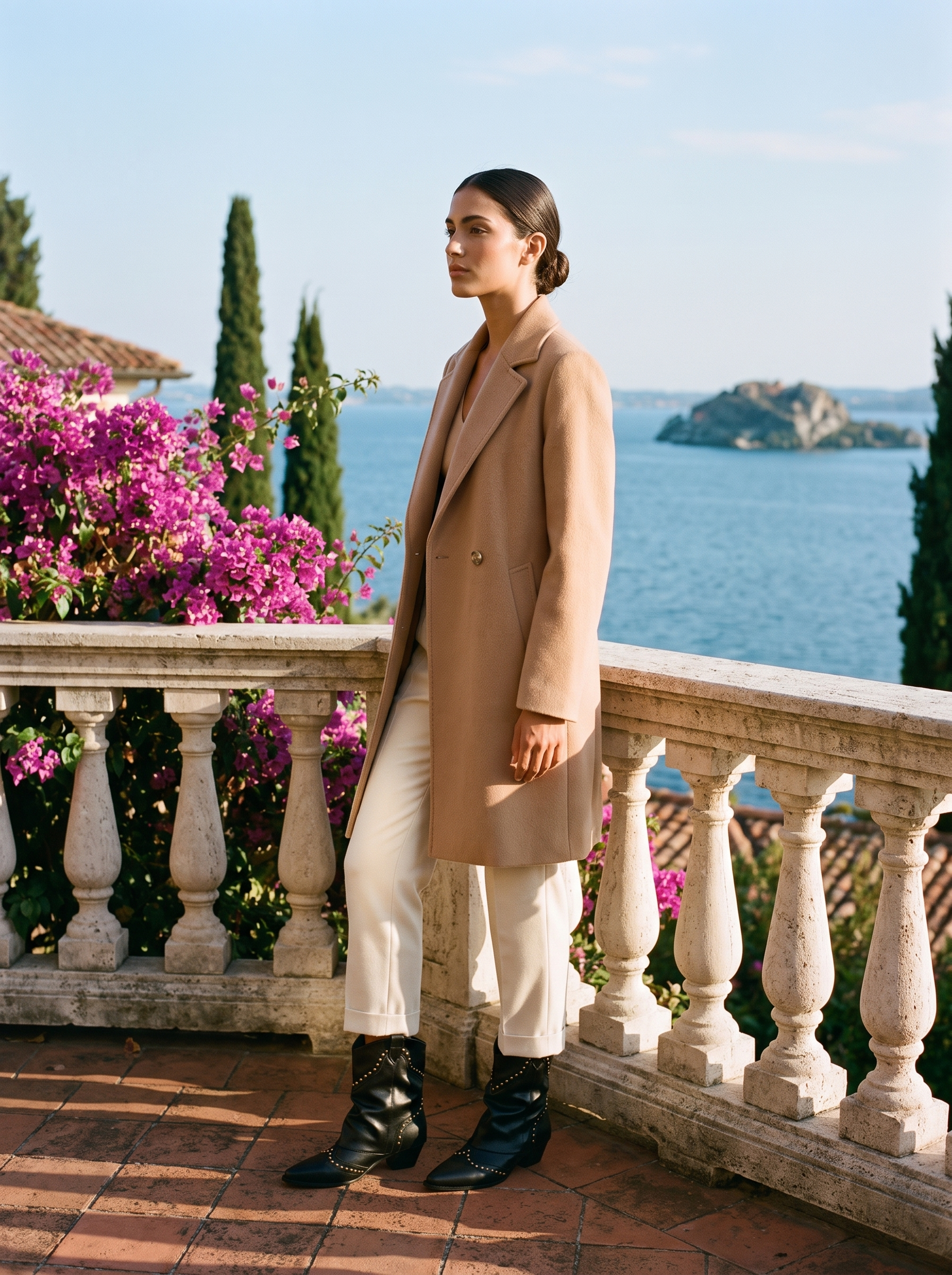 Woman in a camel coat and cream trousers wearing black studded western ankle boots on a Lake Como terrace — Aveloire