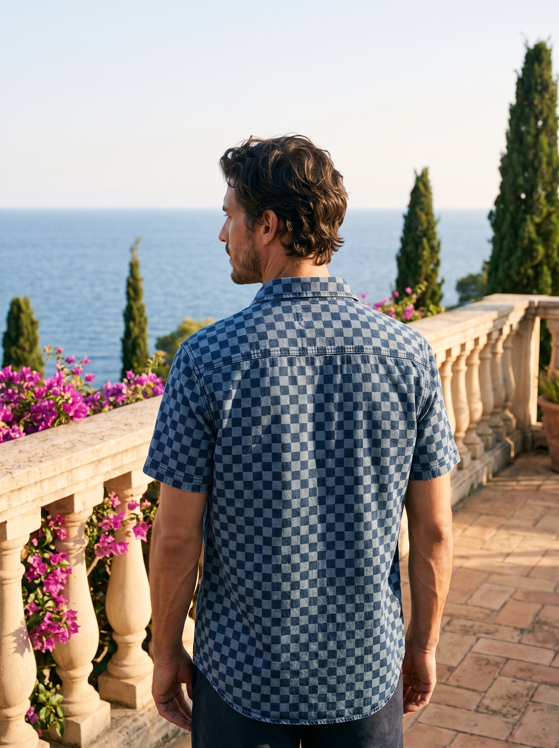 Back view of a man in a navy checkerboard denim shirt overlooking Lake Como — Aveloire