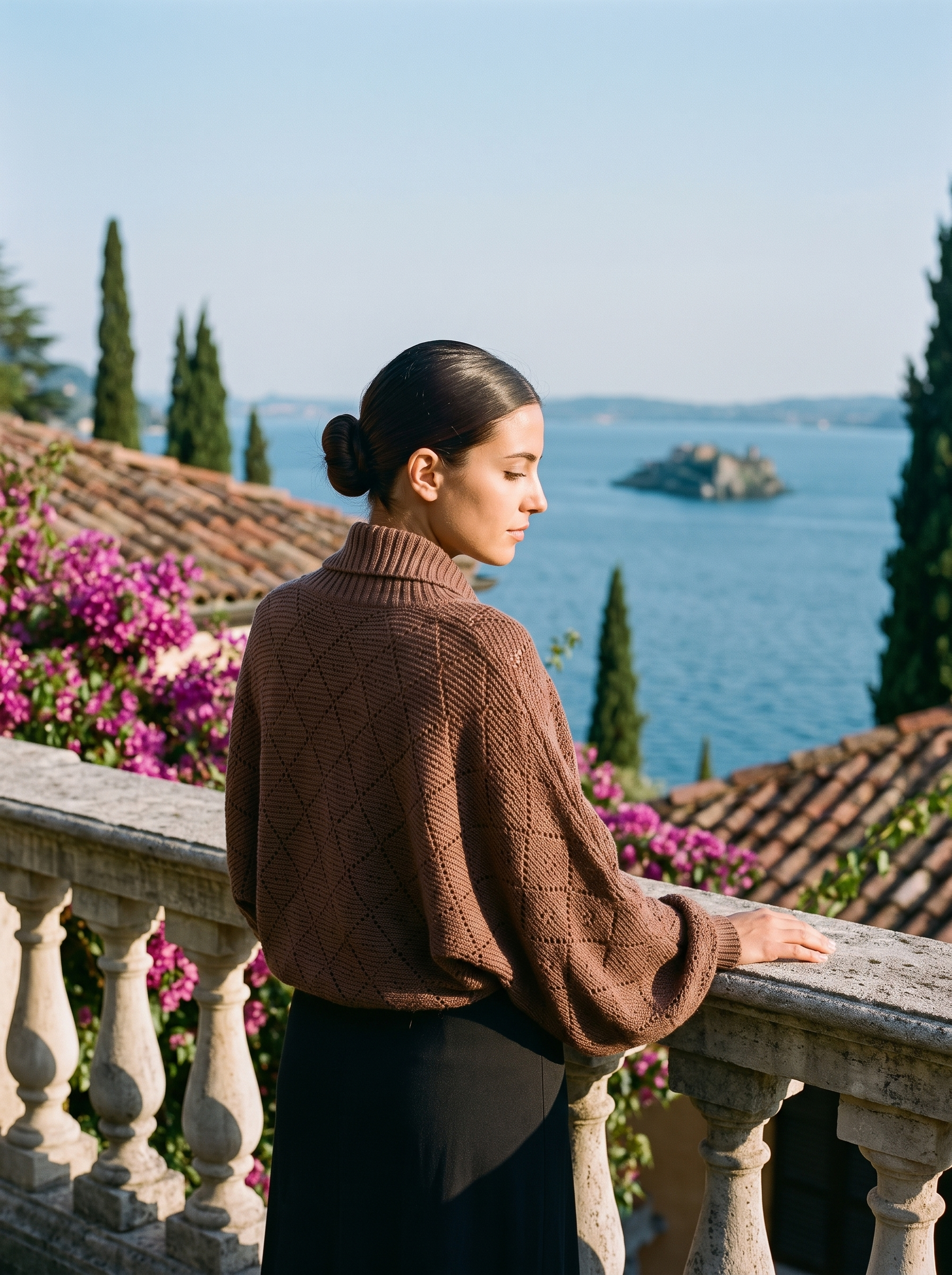 Back view of a cocoa brown cropped batwing knit shrug cardigan on a Lake Como terrace — Aveloire